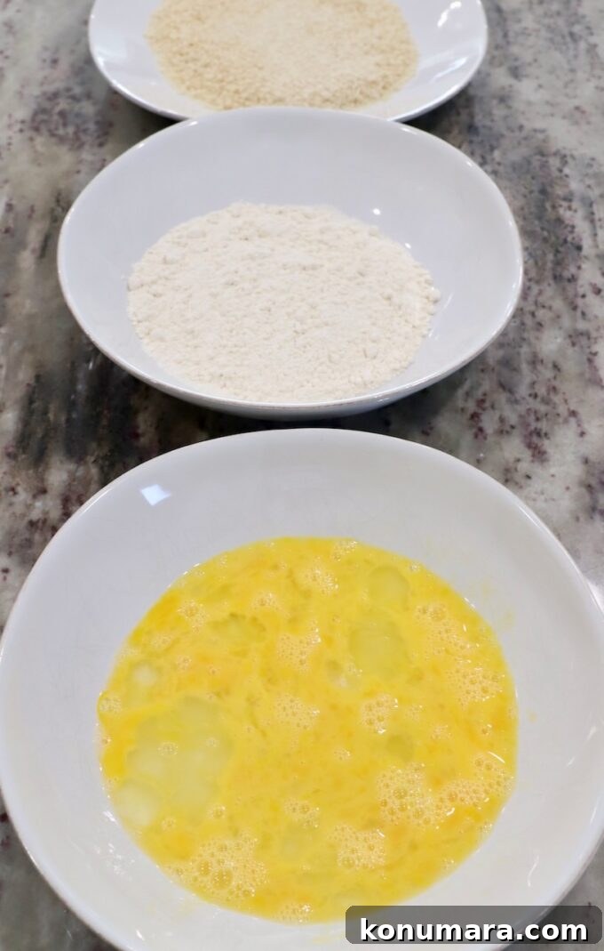 three bowls on countertop, one with whisked egg, one with flour and one with breadcrumbs