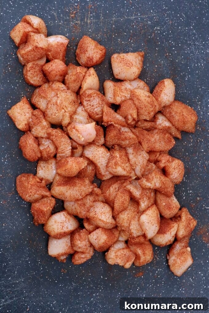 cubes of chicken breasts tossed with seasoning on cutting board