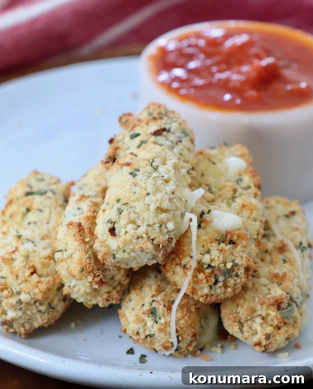 cooked mozzarella sticks stacked up on plate with small bowl of marinara sauce