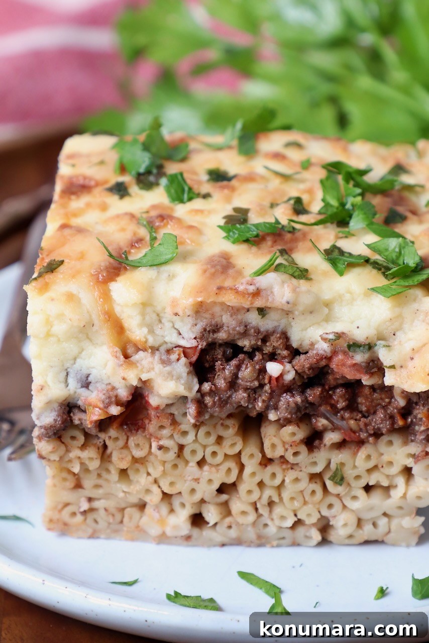 piece of cooked pastitsio on plate, topped with fresh chopped parsley