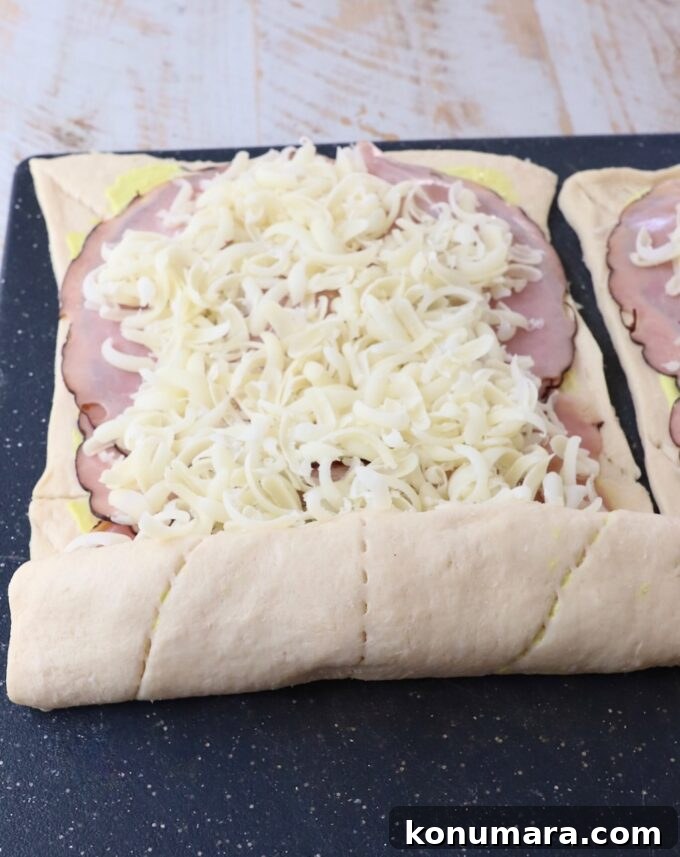 Crescent roll dough rolled up over ham and swiss cheese on a cutting board