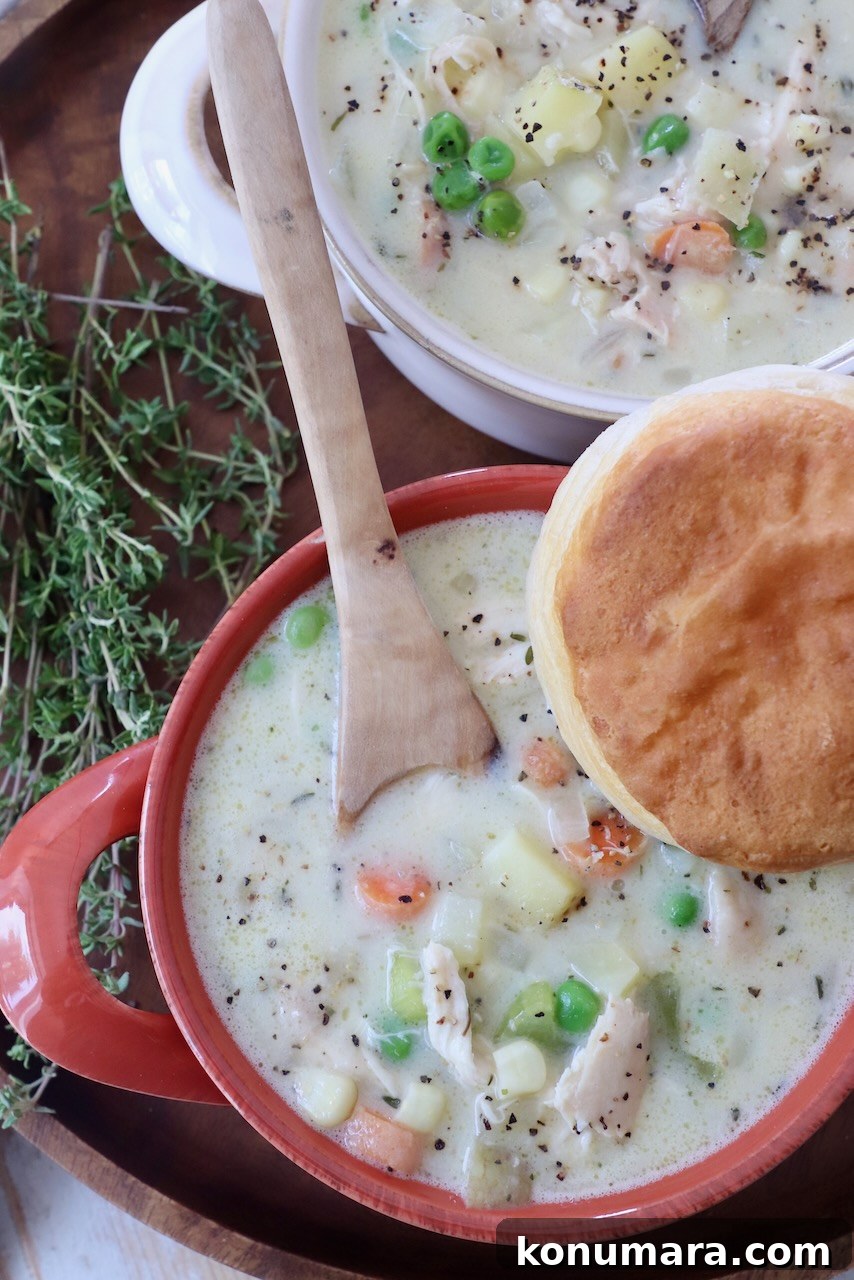 chicken pot pie soup in bowls with wooden spoon, topped with a biscuit
