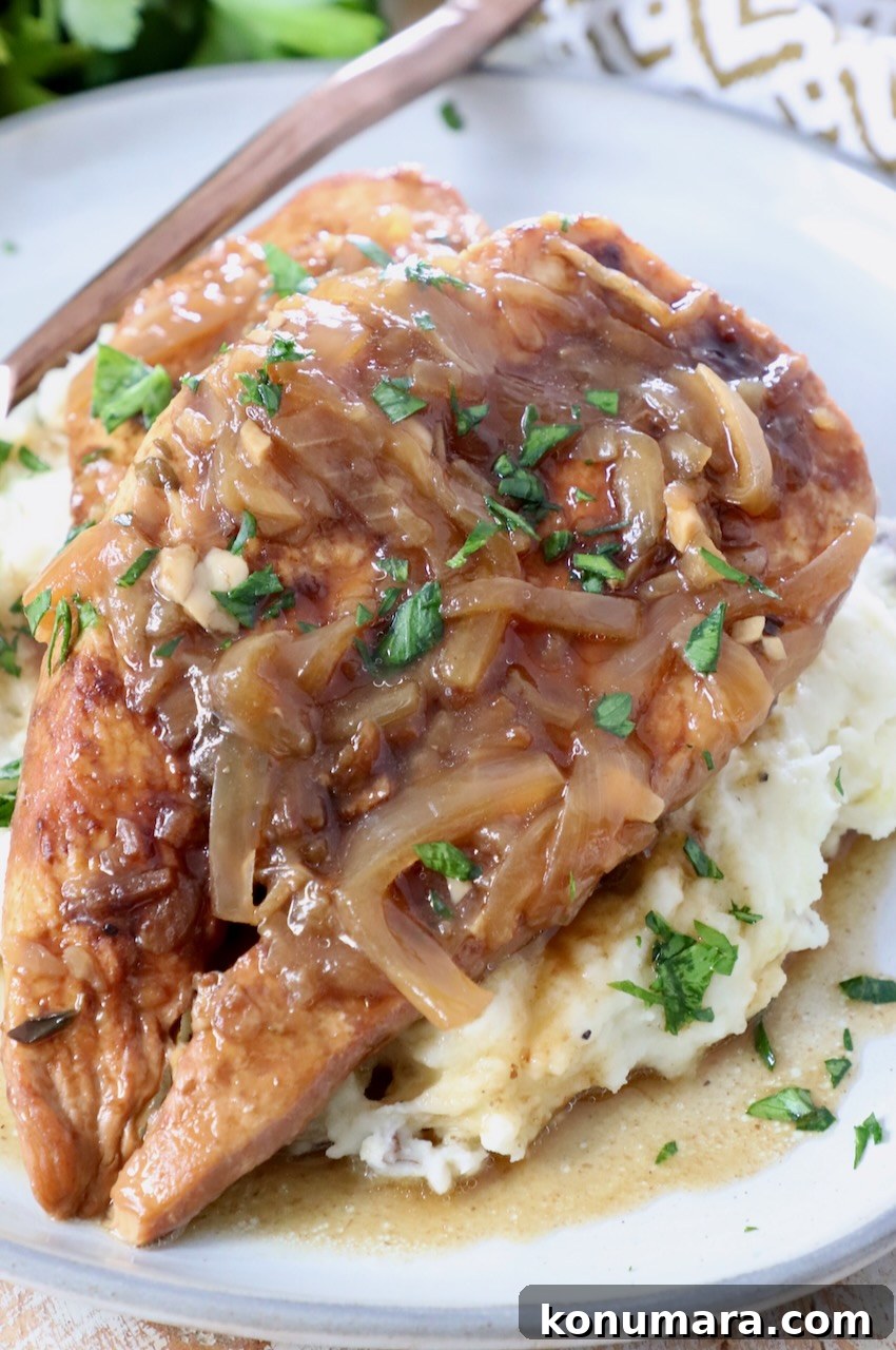 cooked chicken breasts with caramelized onion gravy on top of mashed potatoes on plate