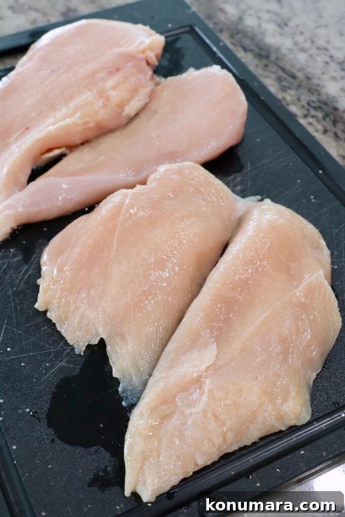 raw chicken breasts sliced in half on cutting board