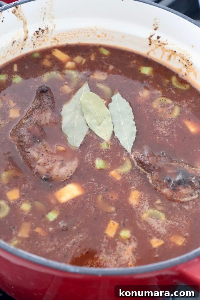 short ribs in liquid in dutch oven with bay leaves on top