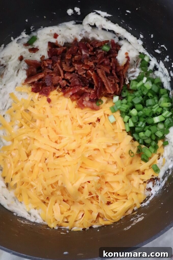 Loaded Mashed Potatoes Recipe with Bacon and Cheddar 6 mashed potatoes in pot topped with shredded cheddar cheese, chopped cooked bacon and diced green onions