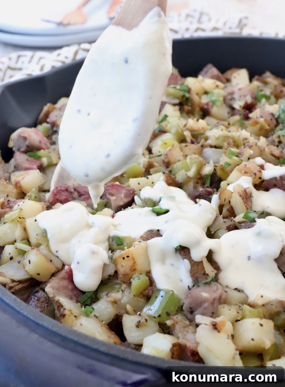 Skillet Philly Cheesesteak Hash with Peppers and Onions 9 cheese sauce in spoon drizzled over potato hash in skillet