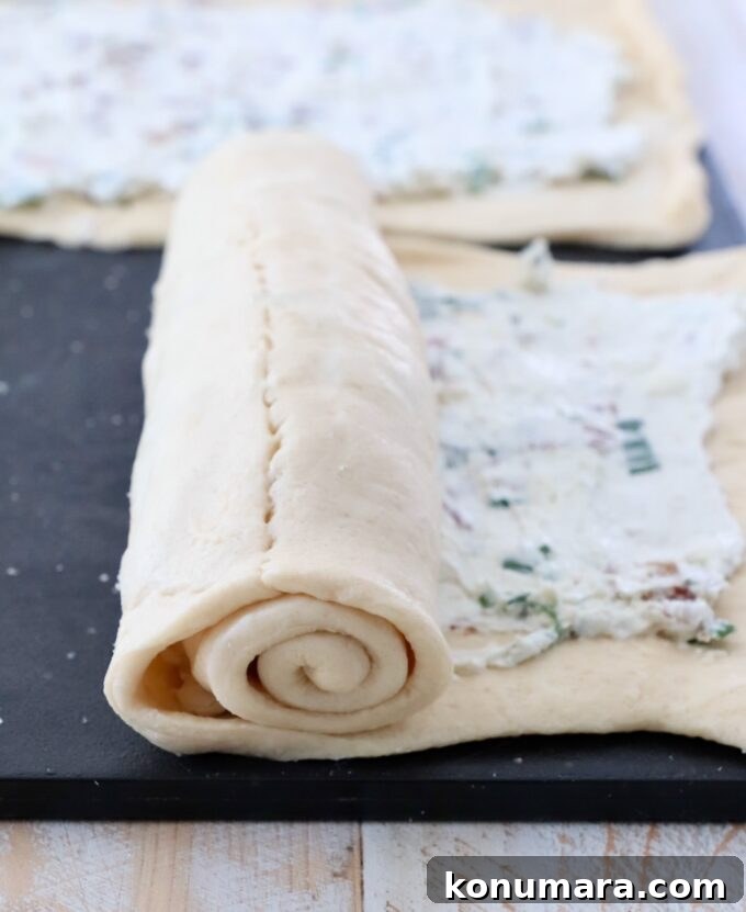 crescent roll dough rolled up over cream cheese filling on cutting board