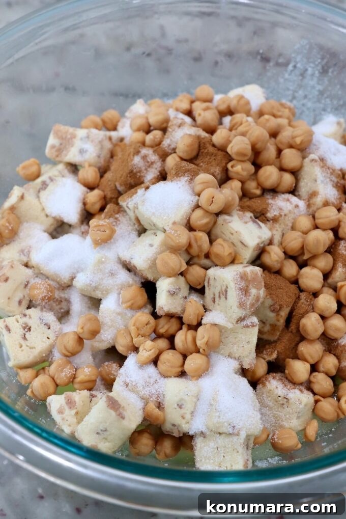 diced up cinnamon rolls in a large glass bowl topped with sugar, cinnamon and caramel bits