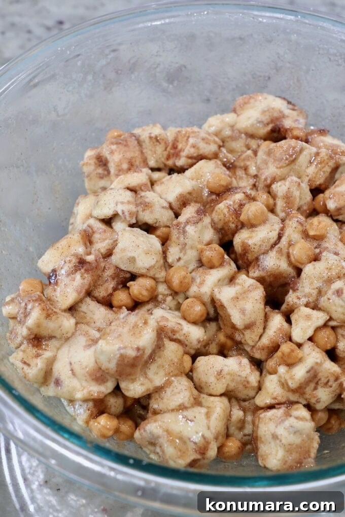 diced up cinnamon rolls in a large glass bowl tossed with melted butter, cinnamon, sugar and caramel bits