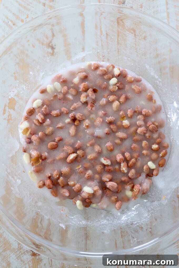 raw peanuts combined with corn syrup and sugar in a large glass bowl