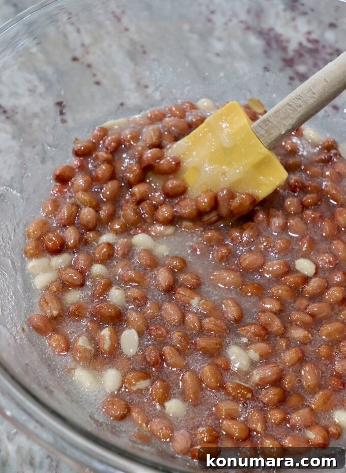 spatula stirring microwaved sugar, corn syrup and raw peanuts together in a large glass bowl