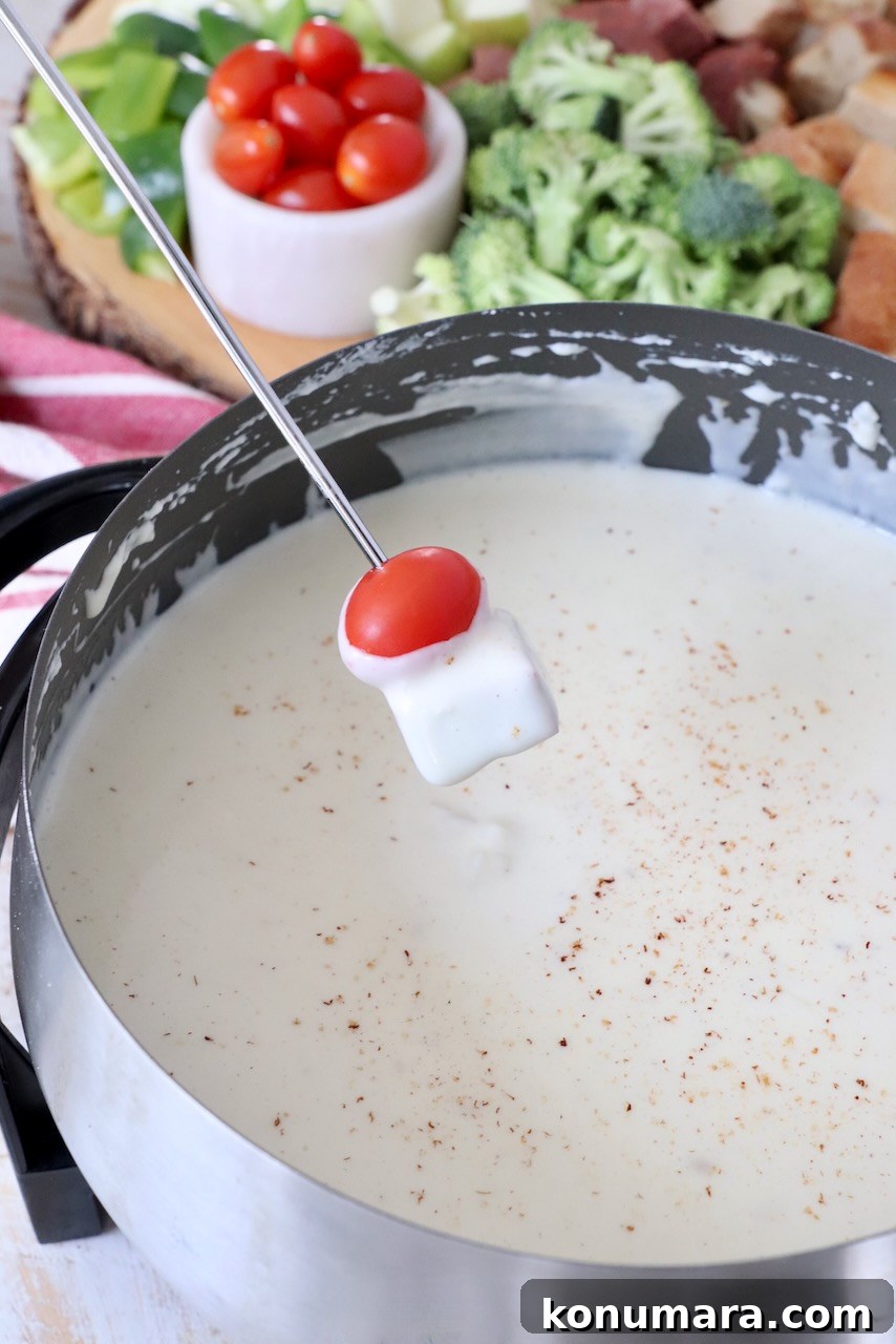 piece of summer sausage and cherry tomato dipped into cheese fondue