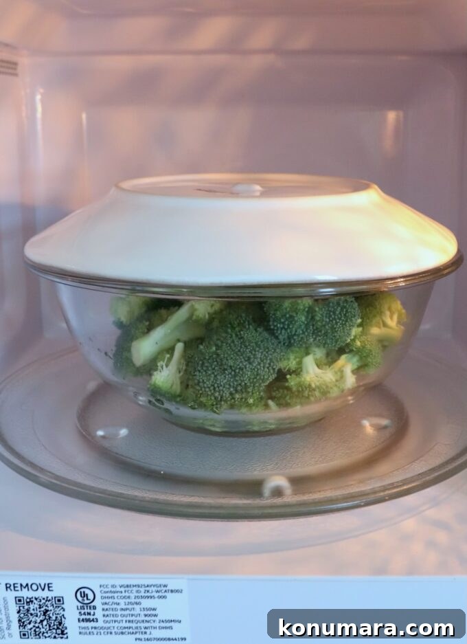broccoli in bowl in microwave with a plate on top