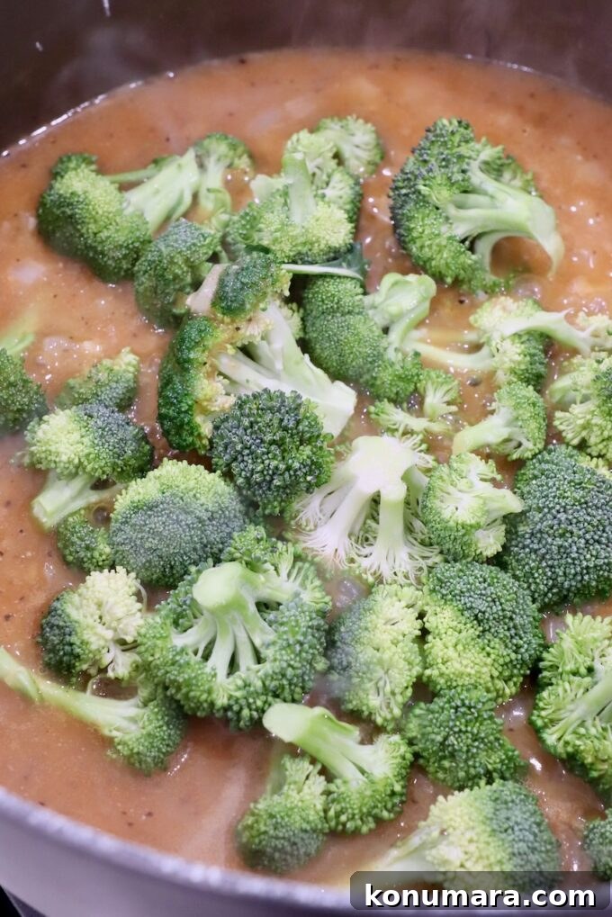 raw broccoli florets in pot with seasoned chicken broth