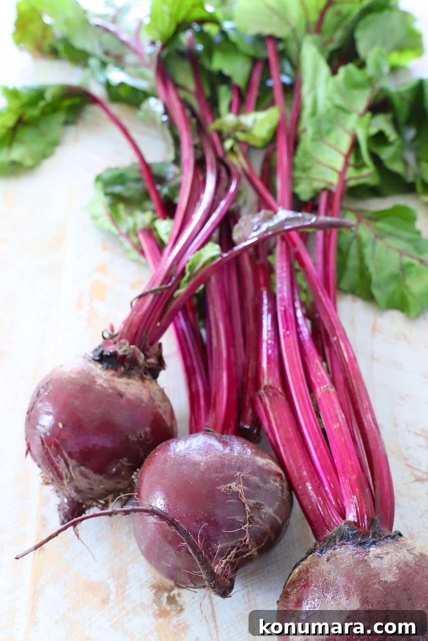 How to Cook Beets: Roast, Boil, and Sauté 2 raw beets with the stems and greens attached on white wood board