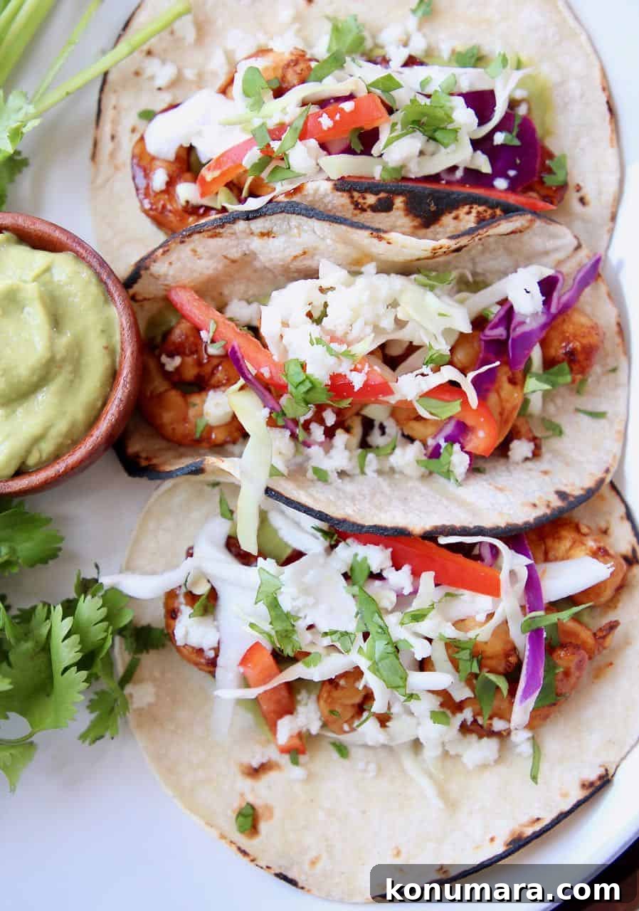 Overhead image of three shrimp tacos on plate with a side of avocado salsa