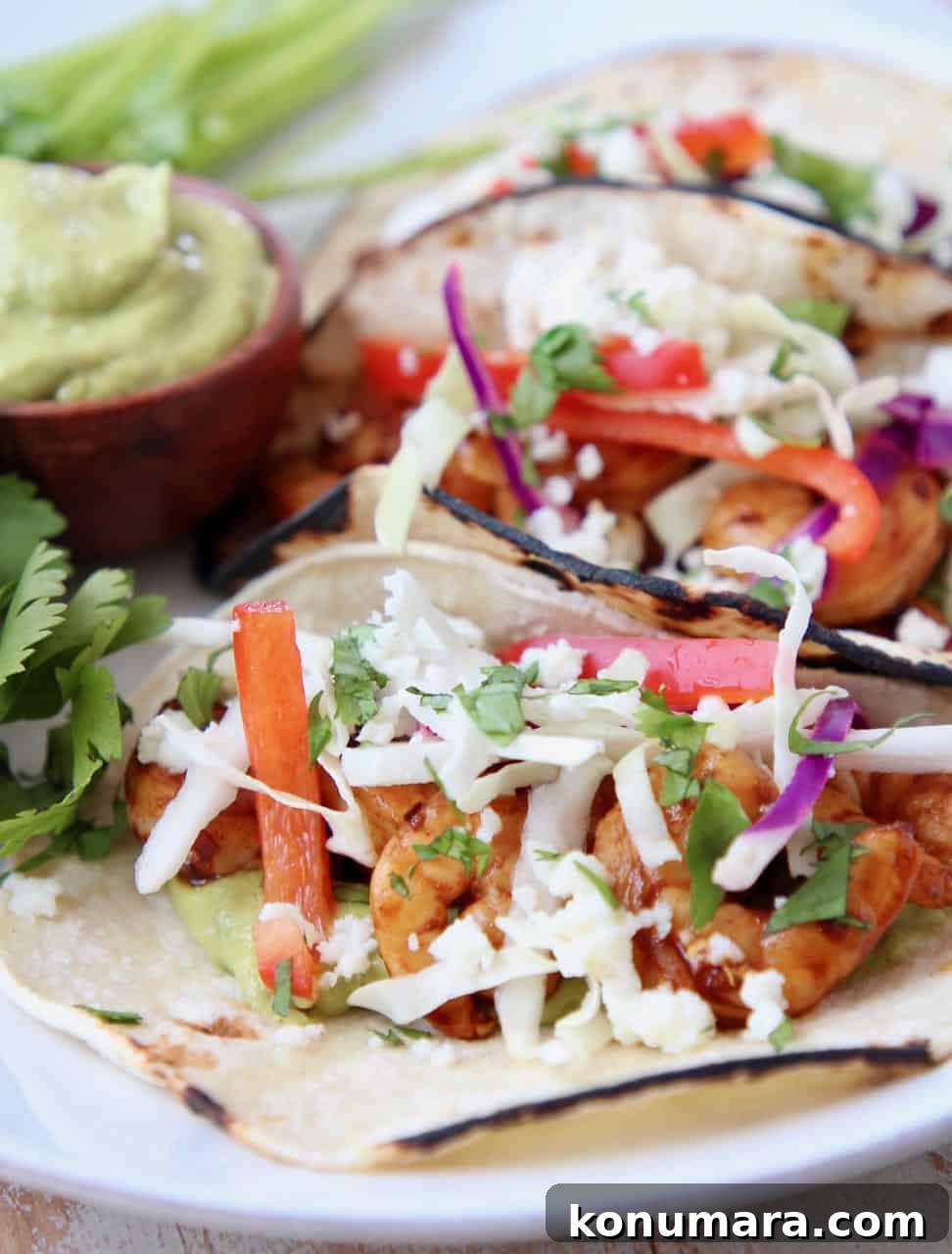 Tacos filled with shrimp, slaw and avocado salsa on white plate with fresh cilantro