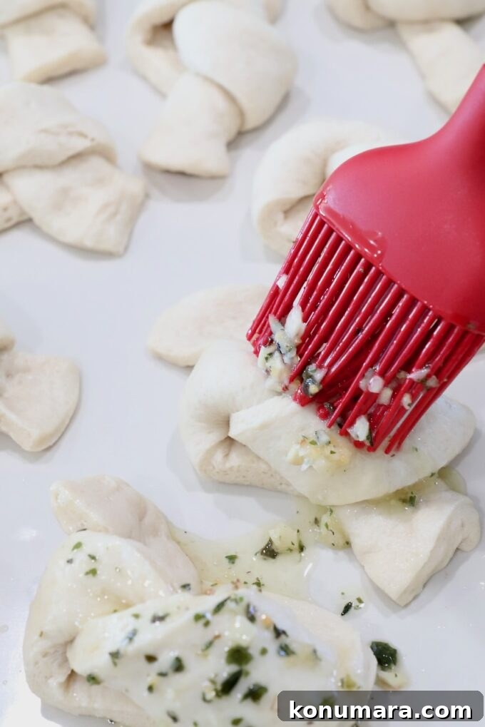 pastry brush brushing seasoned butter on uncooked garlic knots