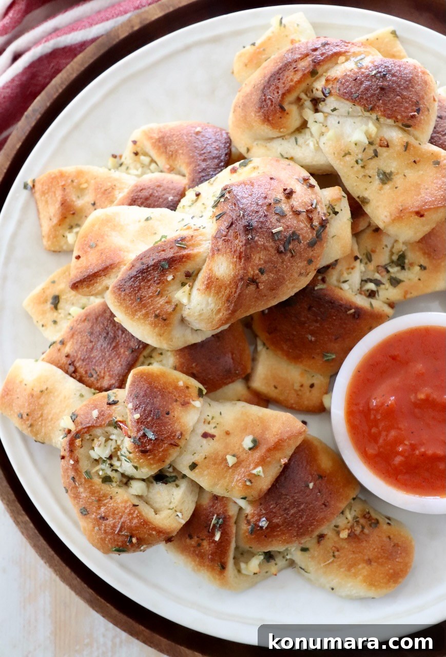 garlic knots stacked up on plate with a small bowl of marinara sauce