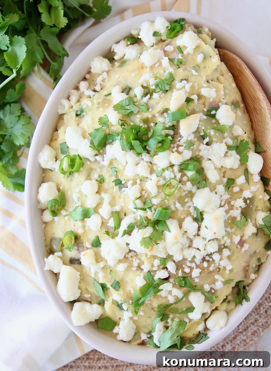 Mashed Mexican Potatoes in a bowl with a wooden spoon, topped with queso fresco and fresh cilantro