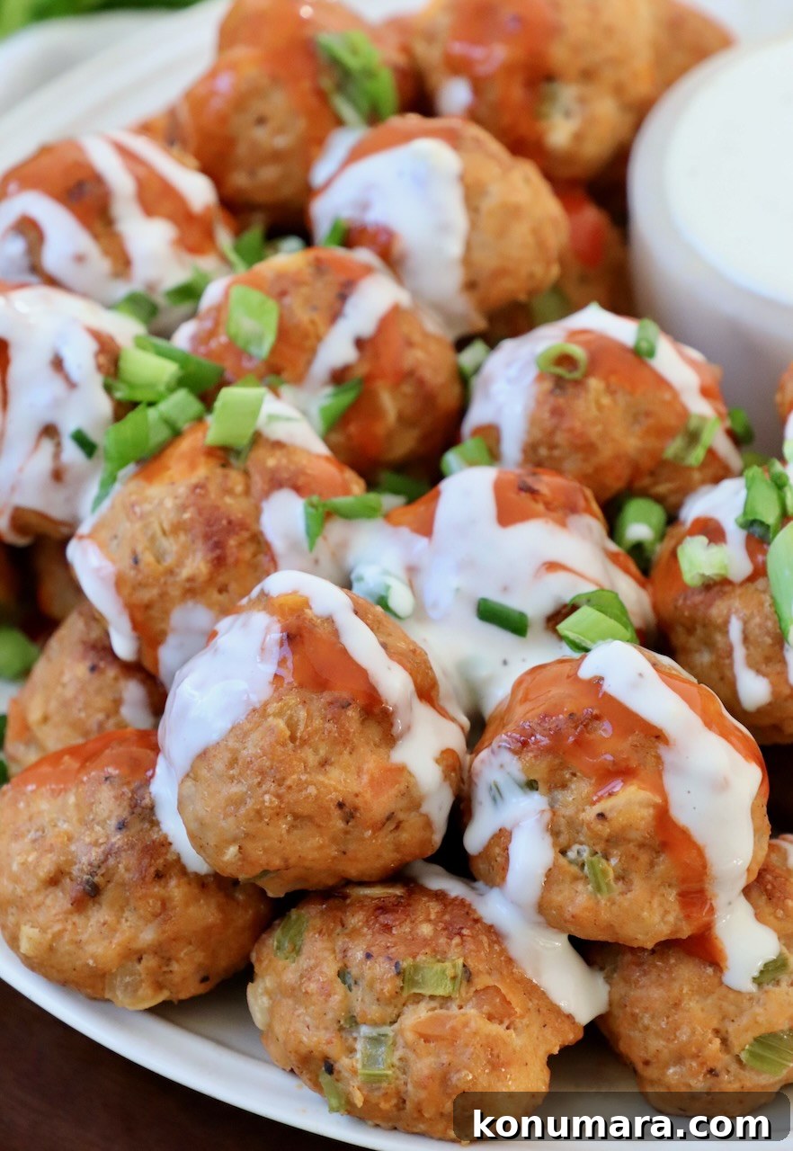 buffalo chicken meatballs stacked up on plate drizzled with blue cheese dressing and buffalo sauce