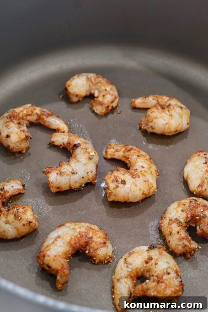 Creamy Cajun Shrimp Pasta with Andouille Sausage 4 seasoned shrimp cooking in pan