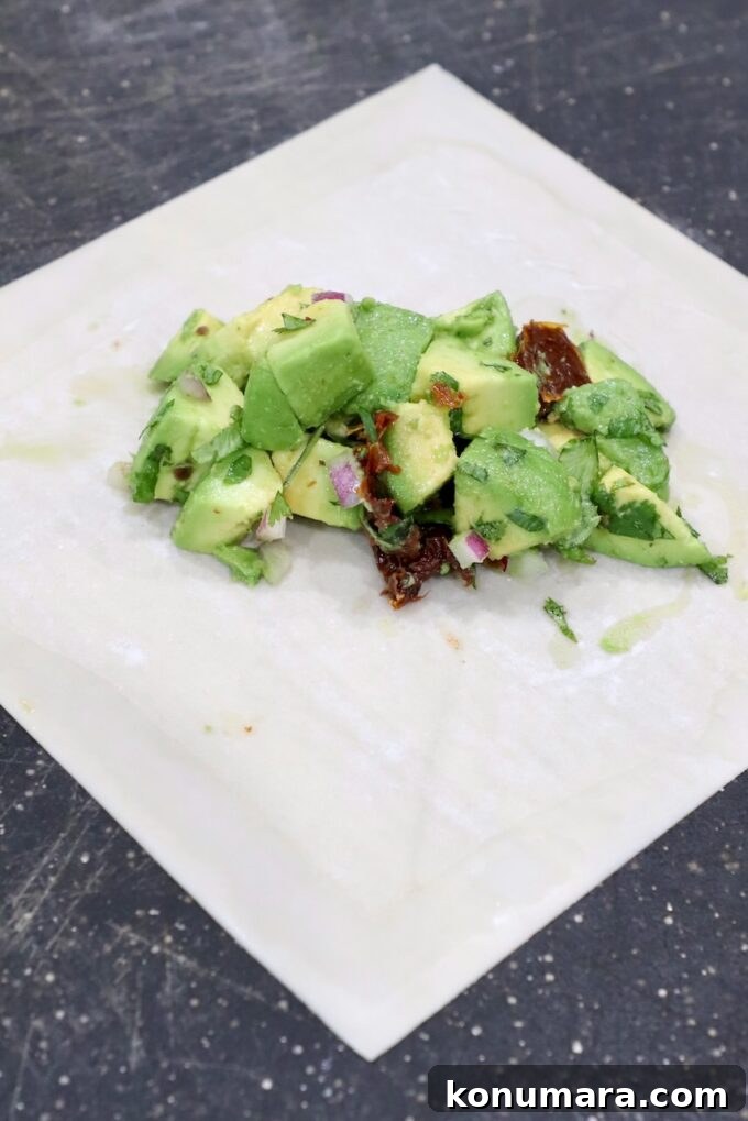 diced avocados in the middle of an egg roll wrapper on a cutting board