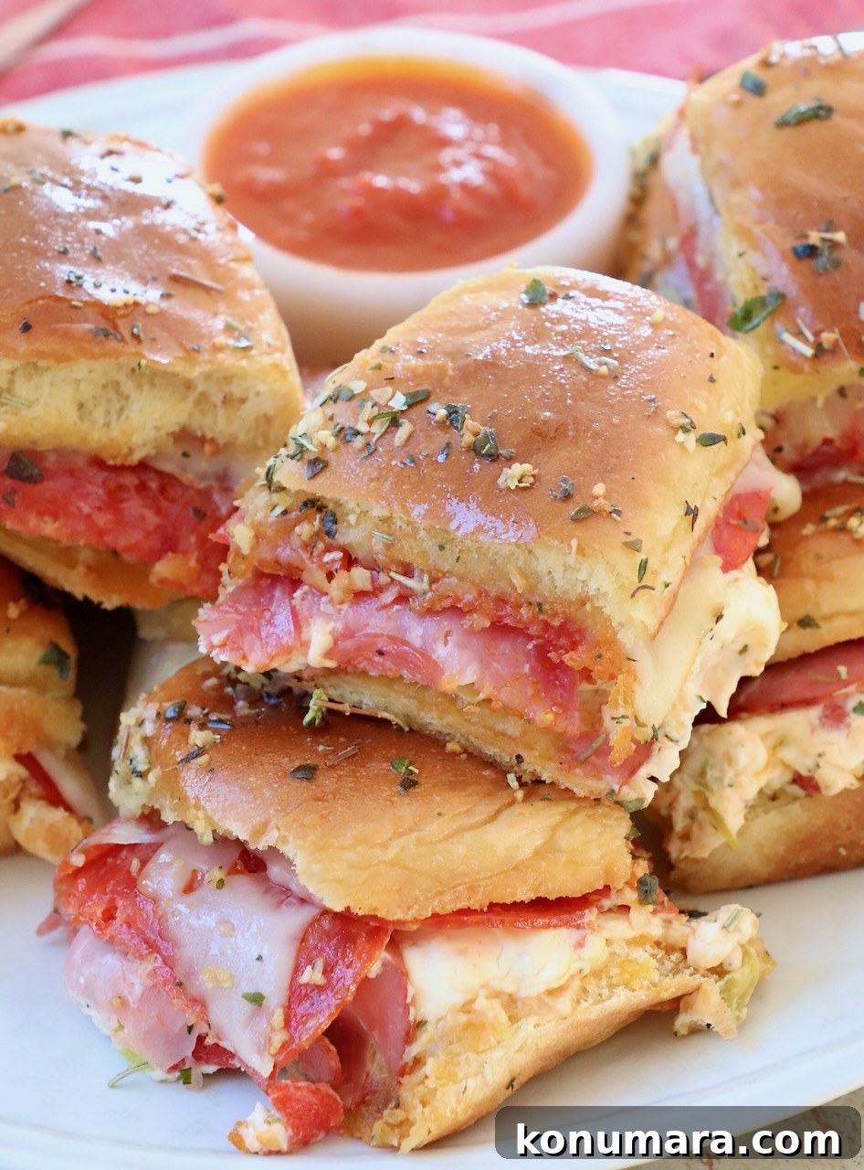 Italian sub sliders stacked up on a plate with a small bowl of marinara sauce on the side
