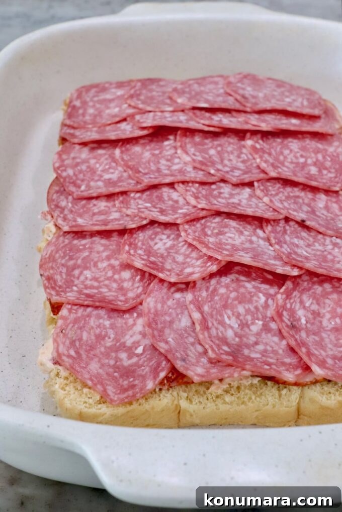 rolls topped with cream cheese and salami in casserole dish