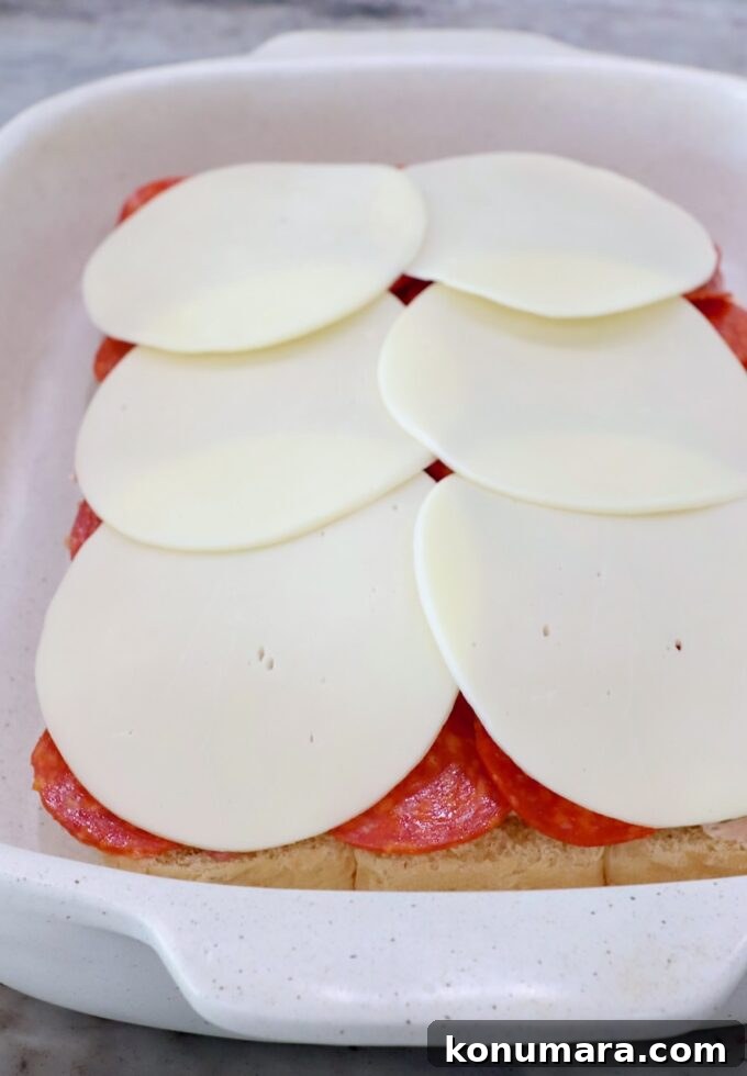 rolls topped with cream cheese, sliced deli meat and provolone cheese in casserole dish