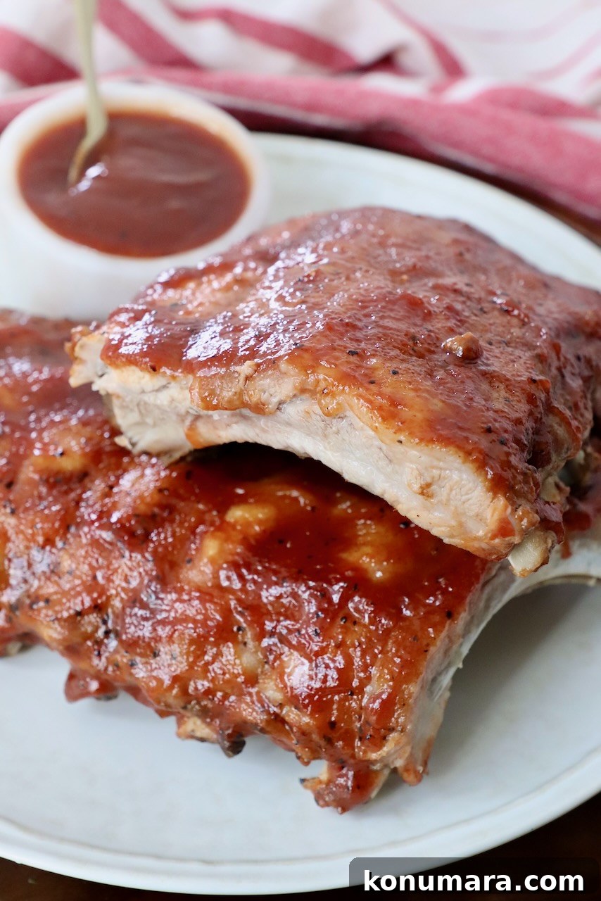 Dry Rub for Ribs: Smoky BBQ Spice Blend 4 cooked baby back ribs stacked up on a plate with a small bowl of bbq sauce on the side