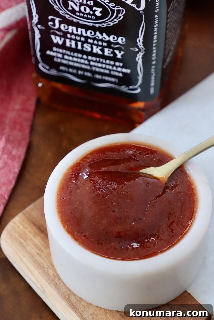 Jack Daniel's BBQ Sauce Recipe: Smoky and Tangy 2 bbq sauce in small bowl with spoon, with bottle of Jack Daniels whiskey behind it