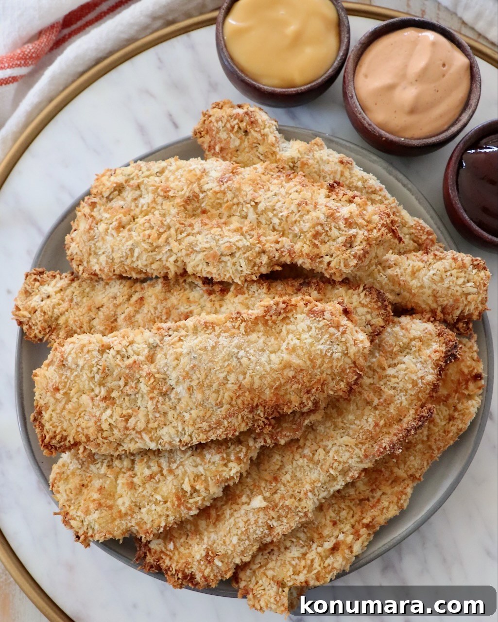 Crispy Air Fryer Chicken Tenders Recipe 2 cooked, breaded chicken tenders stacked up on plate with small bowls of sauce on the side