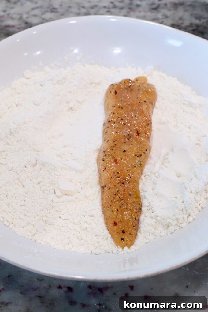 Crispy Air Fryer Chicken Tenders Recipe 7 strip of seasoned chicken in bowl of flour