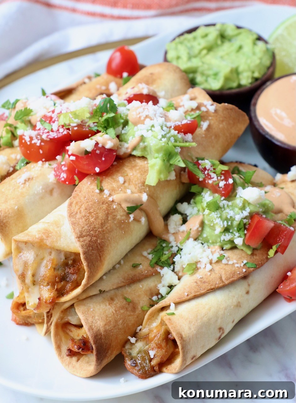 Crispy Air Fryer Taquitos Recipe 12 cooked taquitos stacked up on plate, topped with diced tomatoes, cilantro and cotija cheese