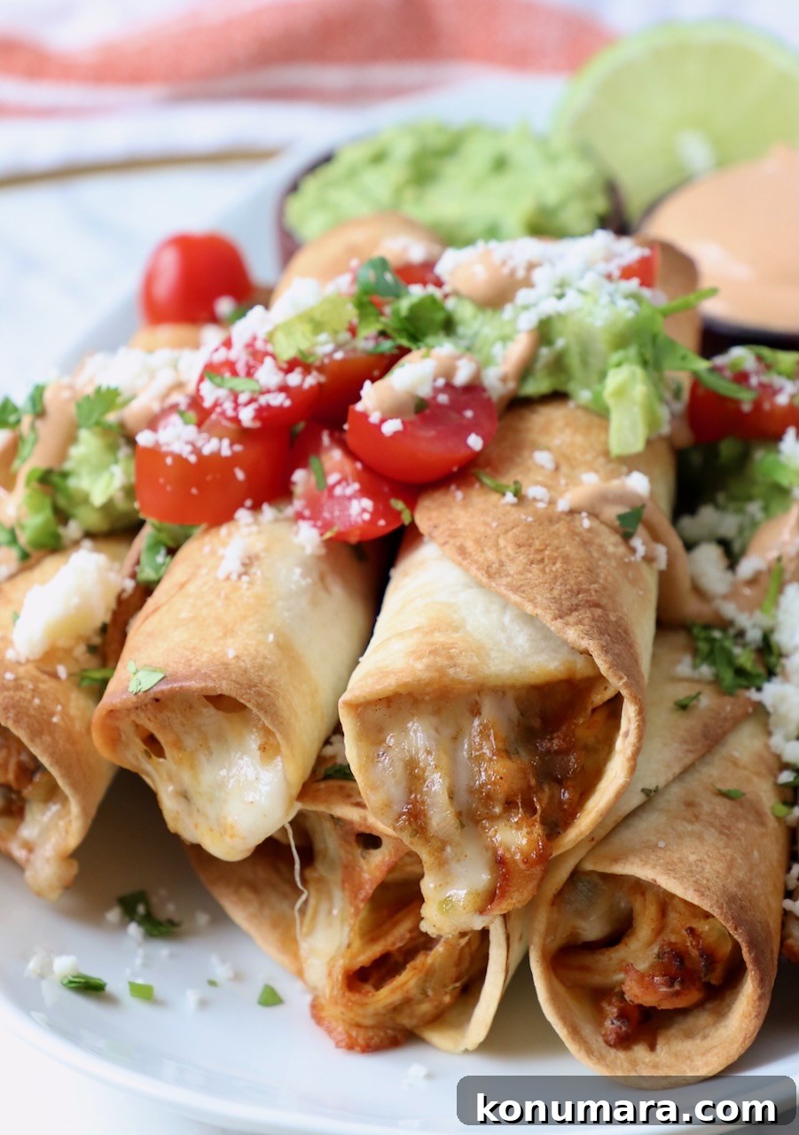 Crispy Air Fryer Taquitos Recipe 13 taquitos stacked up on a plate topped with guacamole and diced tomatoes