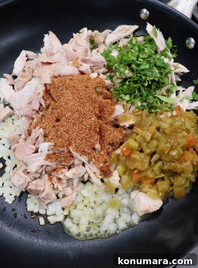 Crispy Air Fryer Taquitos Recipe 5 shredded chicken with diced onions, spices, cilantro and green chiles in a skillet