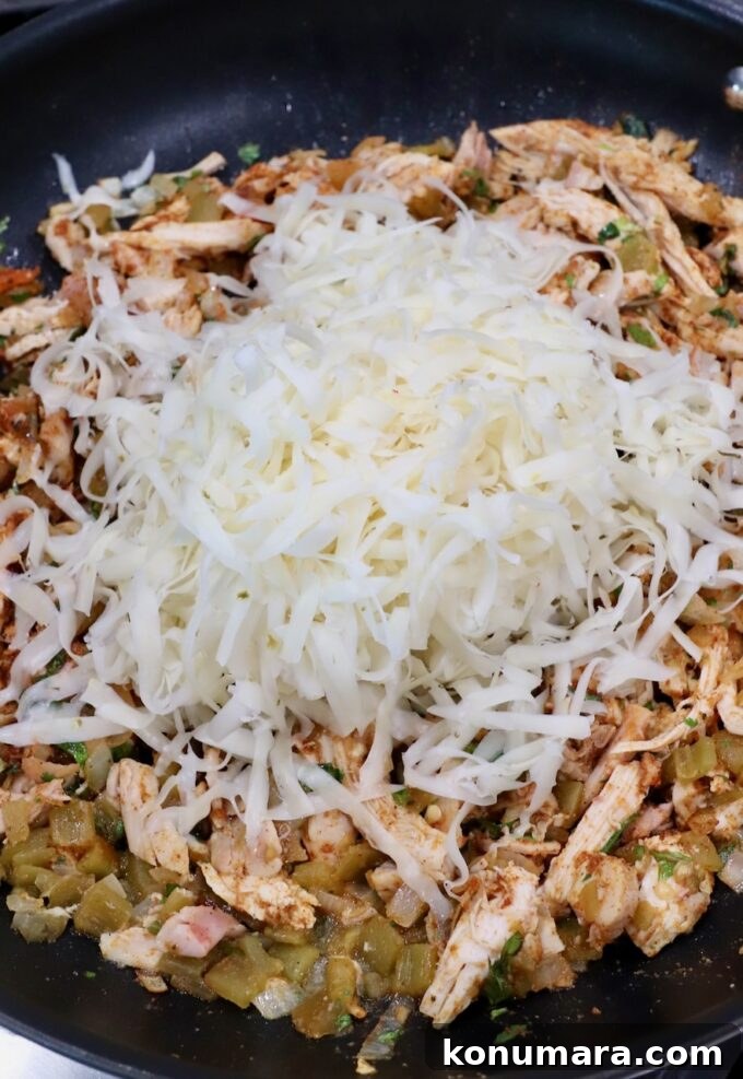 Crispy Air Fryer Taquitos Recipe 7 seasoned shredded chicken in skillet topped with shredded pepper jack cheese
