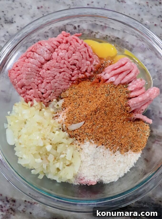 ground pork and beef in bowl with eggs, spices, cooked onions and breadcrumbs