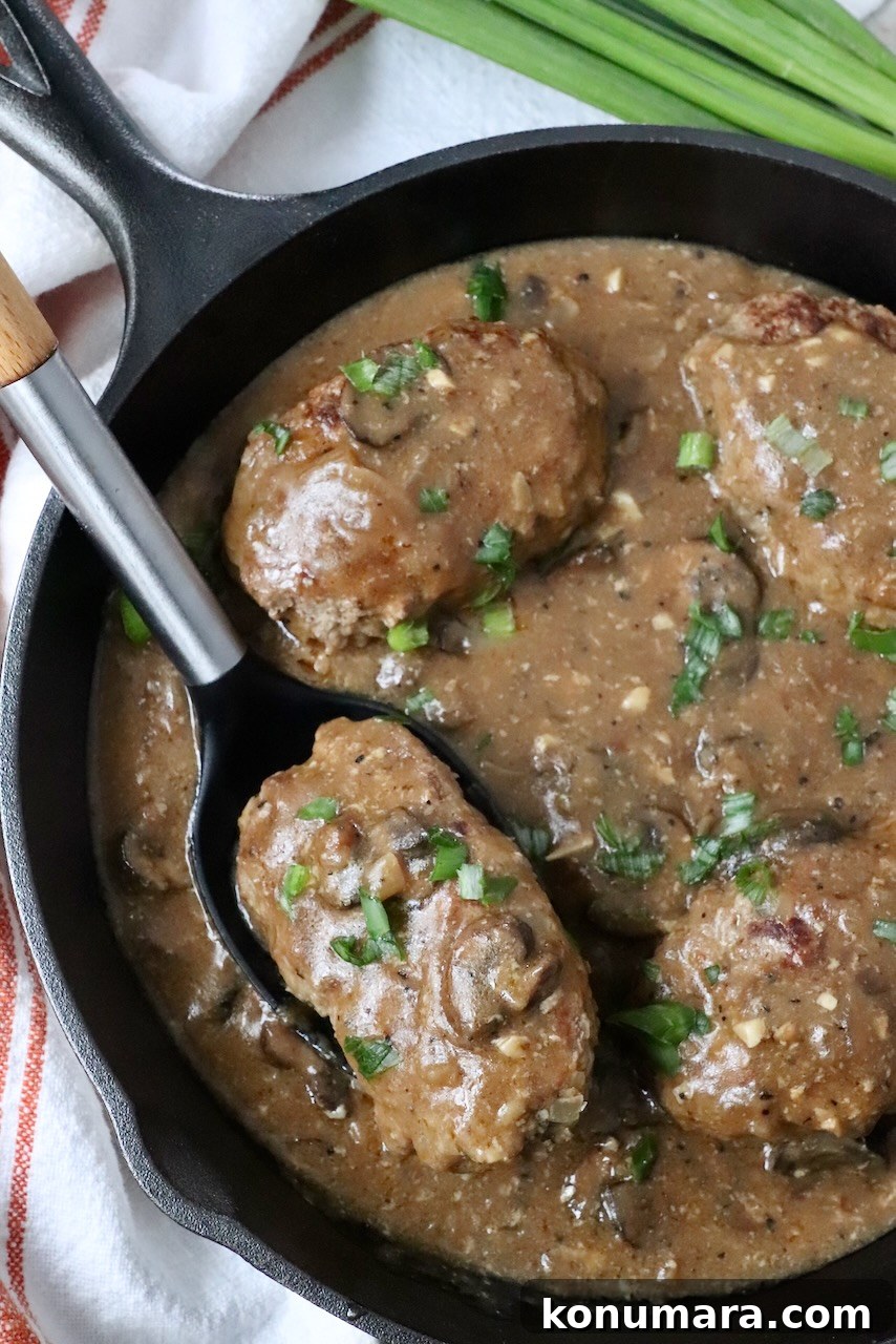 salisbury steak with mushroom gravy in skillet with serving spoon