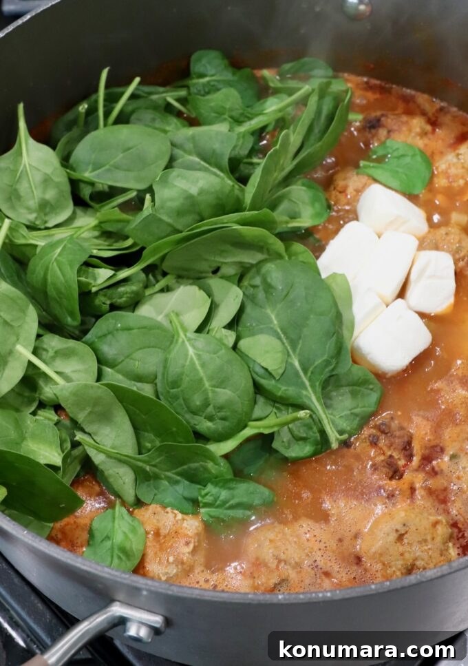Creamy Buffalo Chicken Soup Recipe 7 fresh spinach leaves and cubes of cream cheese in pot of buffalo chicken meatball soup