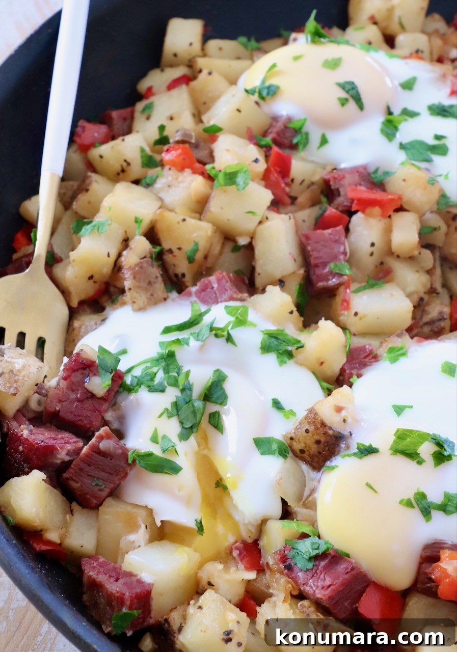 Corned Beef Hash with Crispy Potatoes 2 corned beef hash in skillet with over easy eggs on top and fork on the side