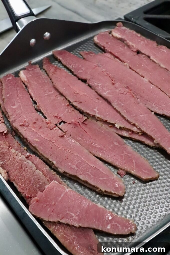 slices of corned beef on griddle pan on stove