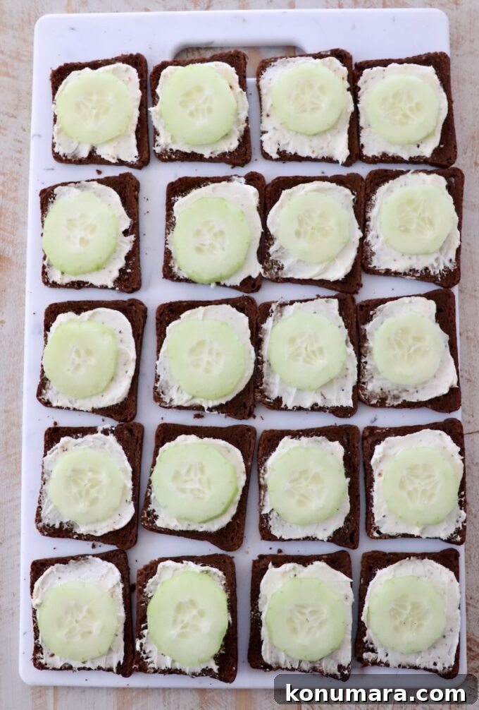 sliced cucumbers on top of cream cheese on cocktail rye bread on cutting board