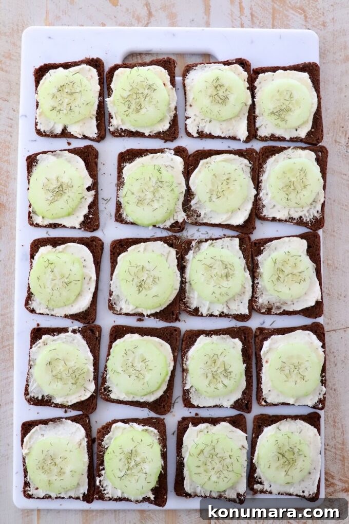 sliced cucumbers topped with dill, on top of cream cheese on cocktail rye bread, on cutting board