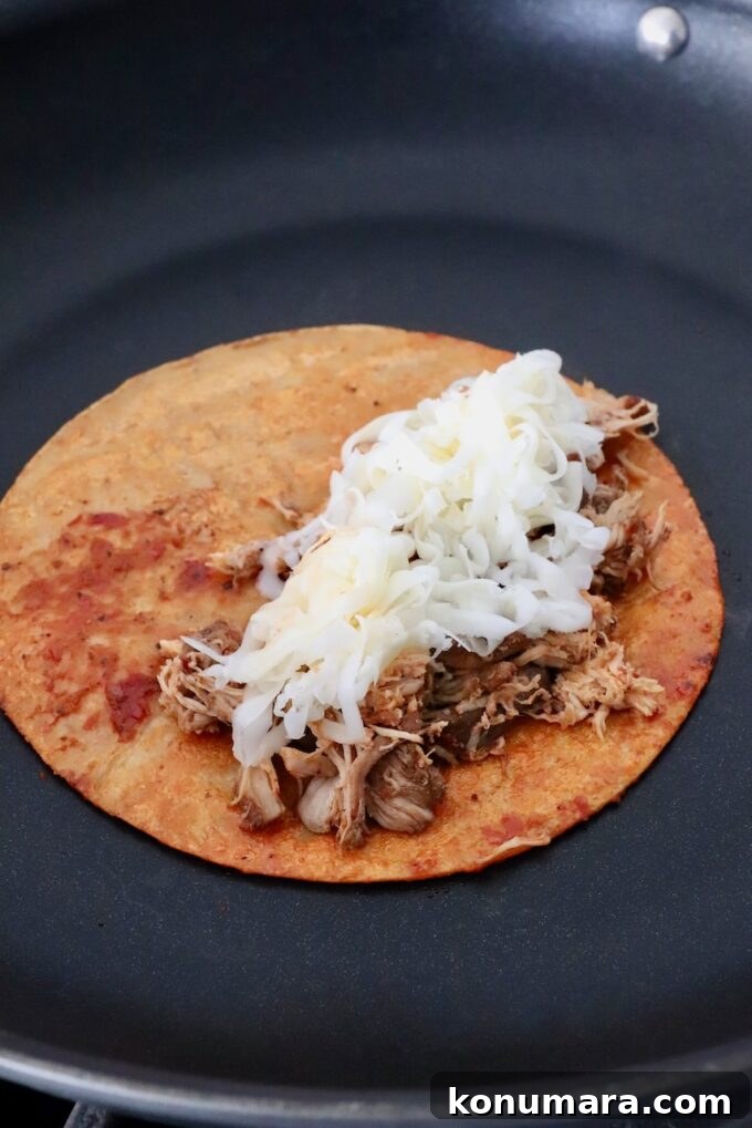 Chicken Birria Tacos with Savory Broth 7 tortilla topped with shredded chicken and cheese in skillet