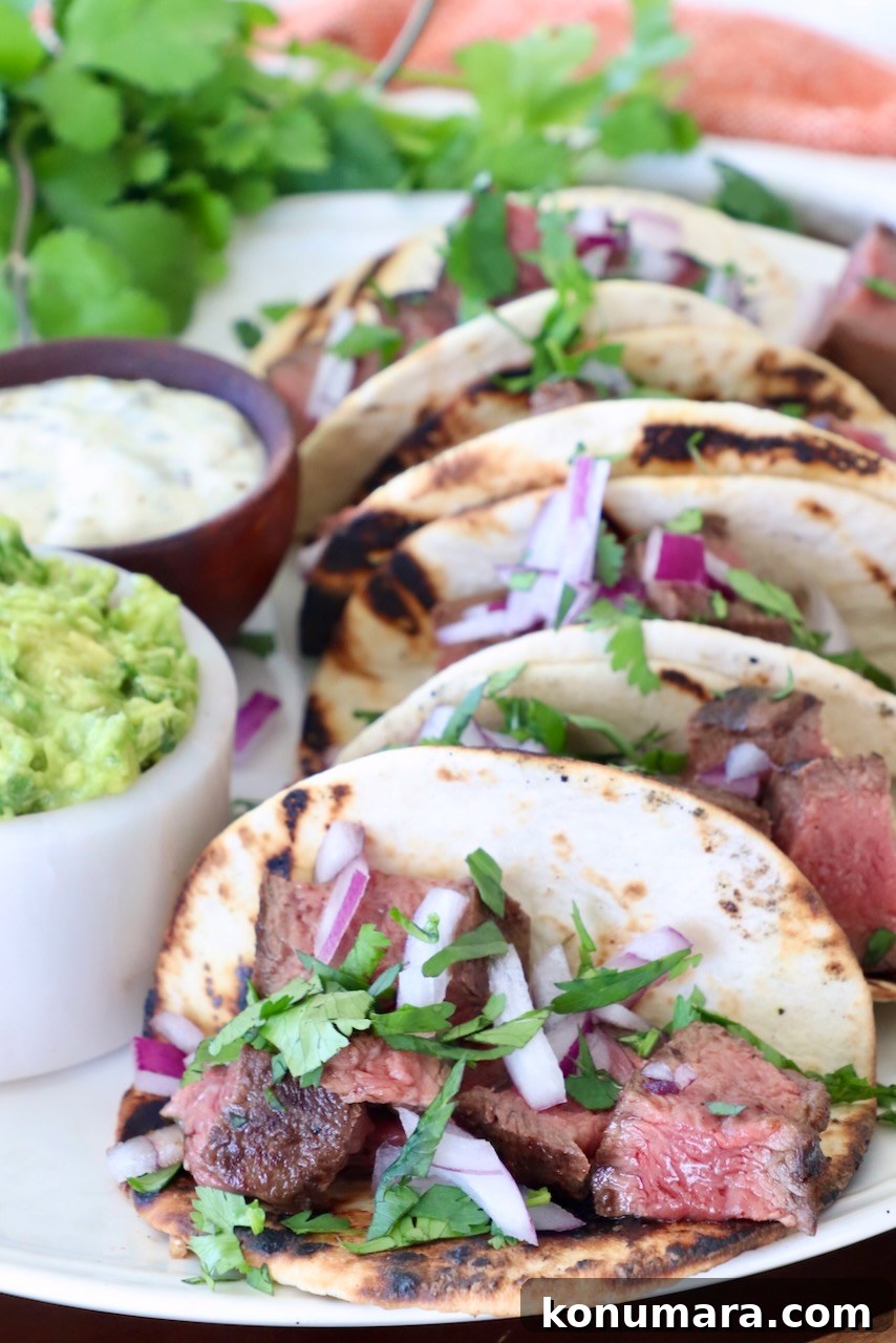 Grilled Flat Iron Steak Tacos with Cilantro Lime Slaw 2 steak tacos on plate with a small bowl of guacamole on the side