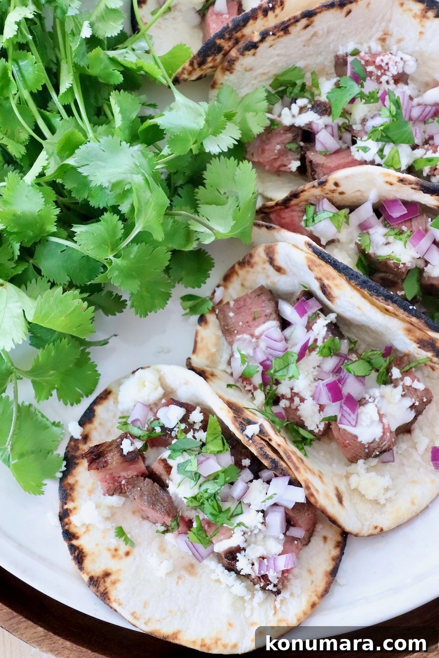 Grilled Flat Iron Steak Tacos with Cilantro Lime Slaw 8 steak tacos on plate with fresh cilantro on the side