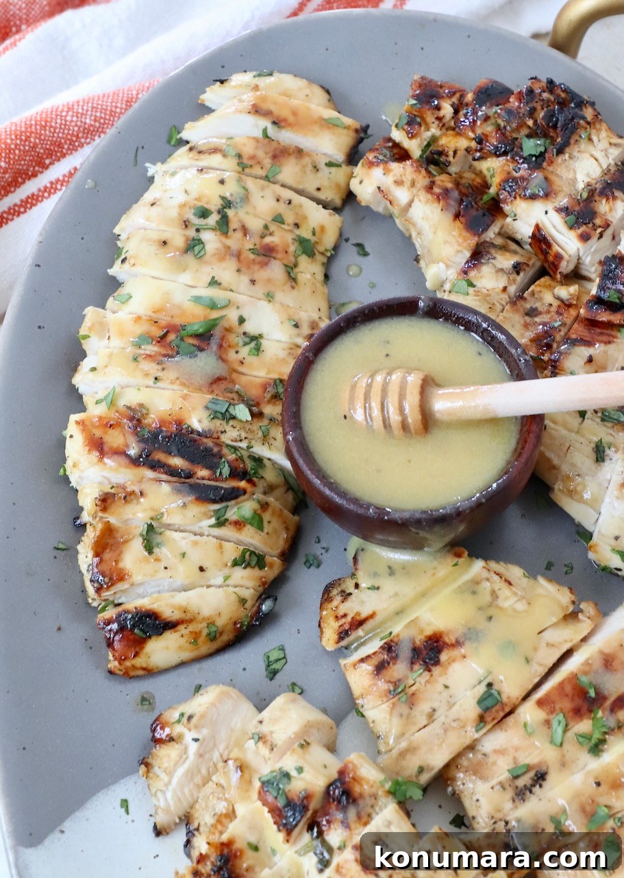sliced grilled chicken on plate with honey mustard dressing in small bowl next to the chicken